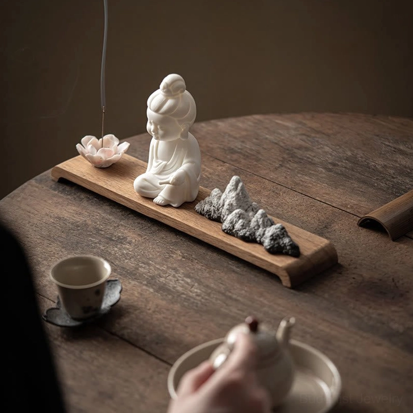 Guanyin Buddhist incense burner set with burning incense and smoke on round wooden tea table with teapot
