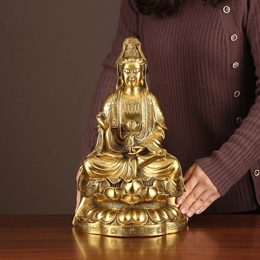 Hand showing size reference of brass Guanyin Avalokitesvara statue on wooden desk, warm golden patina, decorative display