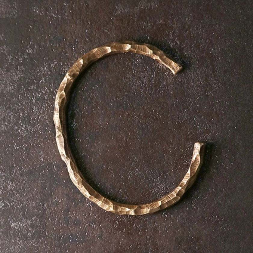 Hammered brass cuff bracelet tilted top-down view, clearly showing open cuff design and intricate textured surface for energy work