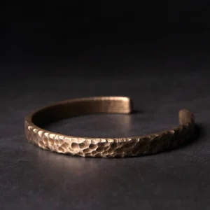 Hammered copper cuff bracelet with open design displayed on dark background, showing antique bronze finish and artisanal texture