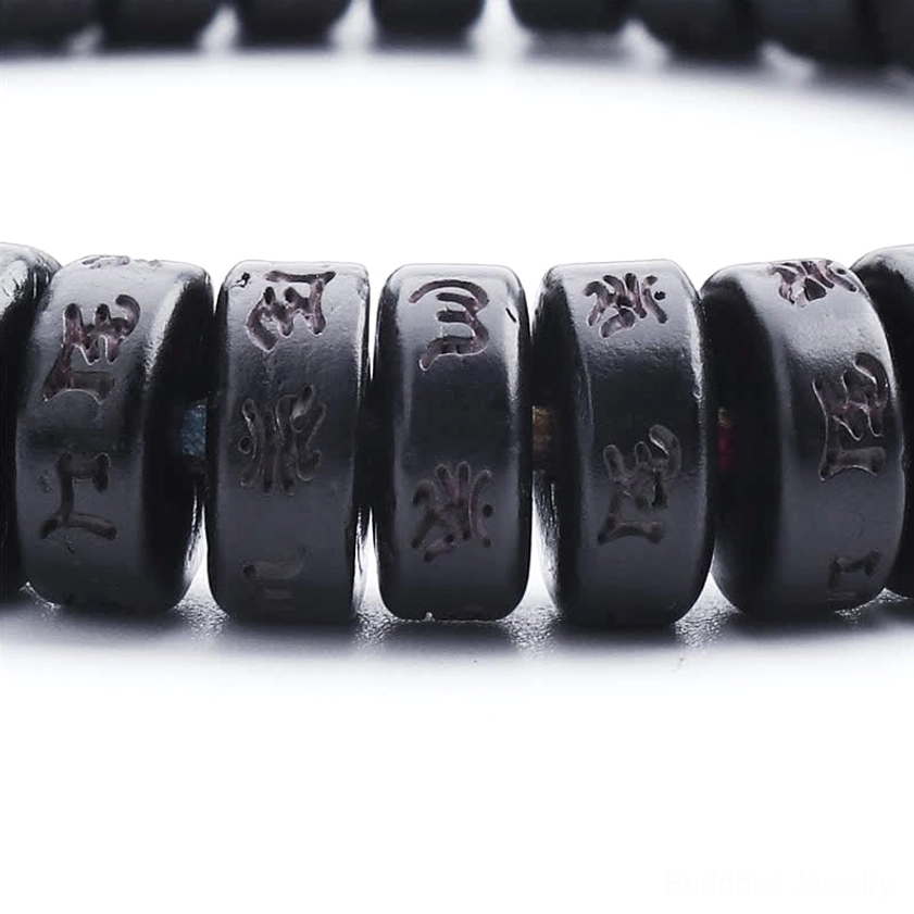 Ultra close-up macro view of hand-engraved mantras on black coconut shell beads with Sanskrit characters