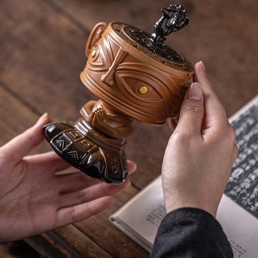 Handcrafted Buddhist incense burner held in hands, two-tone brown and black ceramic finish, low angle view