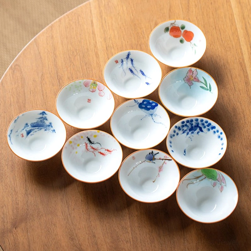 Multiple hand-painted Buddhist porcelain teacups displayed flat lay showing detailed Buddhist artwork and patterns