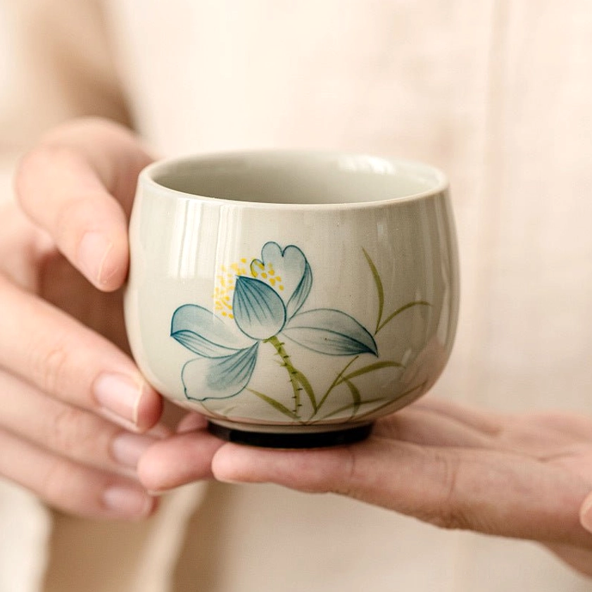 Hand-painted lotus tea cup held in hands showing matte ceramic finish and detailed flower pattern - meditation tea ceremony cup