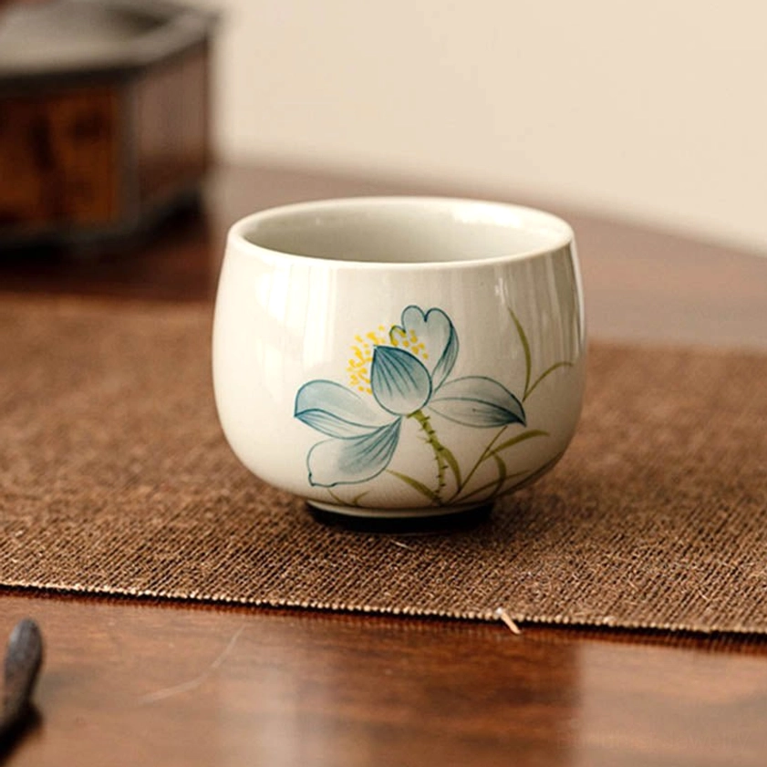 Hand-painted lotus tea cup front side view on wooden table with linen placemat - authentic Buddhist gongfu tea vessel