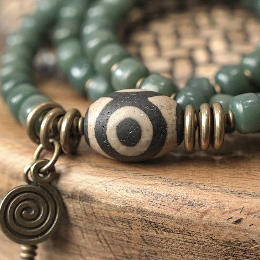 Detailed close-up of hand-painted three-eye dzi bead with bronze coil spacers and spiritual symbolism