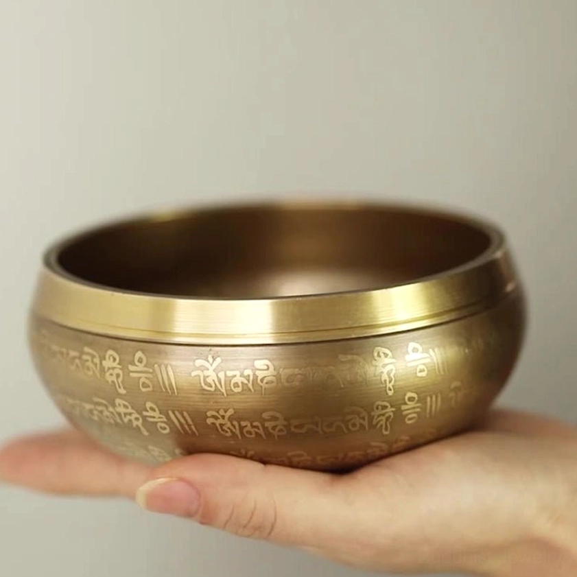 Close-up handheld view of authentic brass singing bowl featuring engraved Buddhist dharma scriptures and traditional sacred symbols on exterior