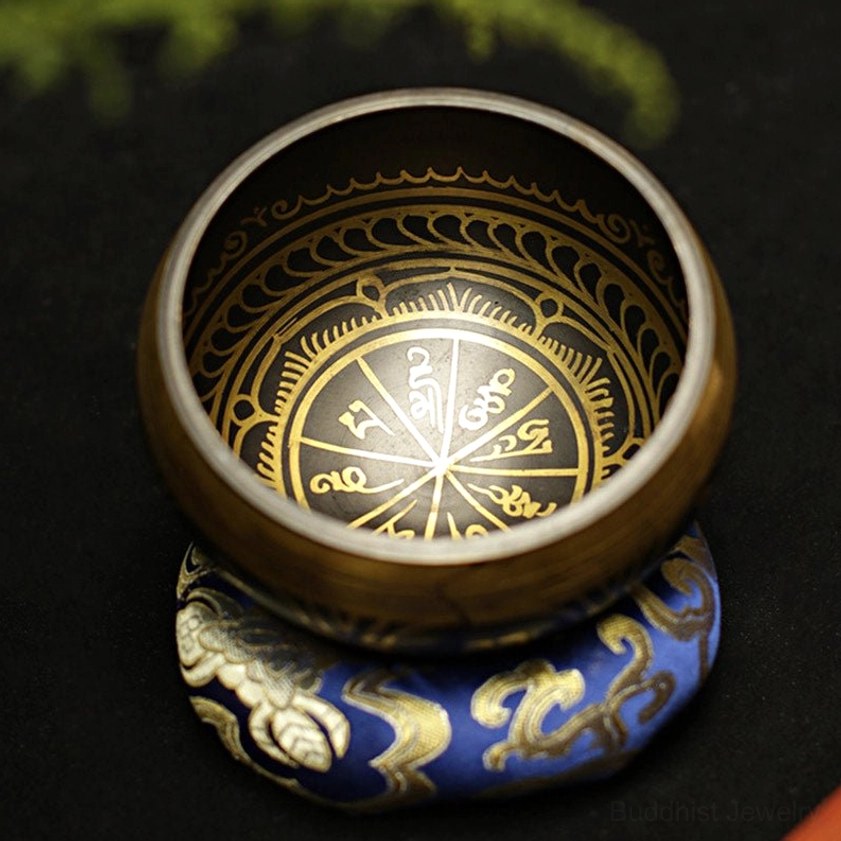 Single Buddhist singing bowl with bronze finish and intricate gold Sanskrit patterns on inner surface, seated on blue embroidered meditation cushion