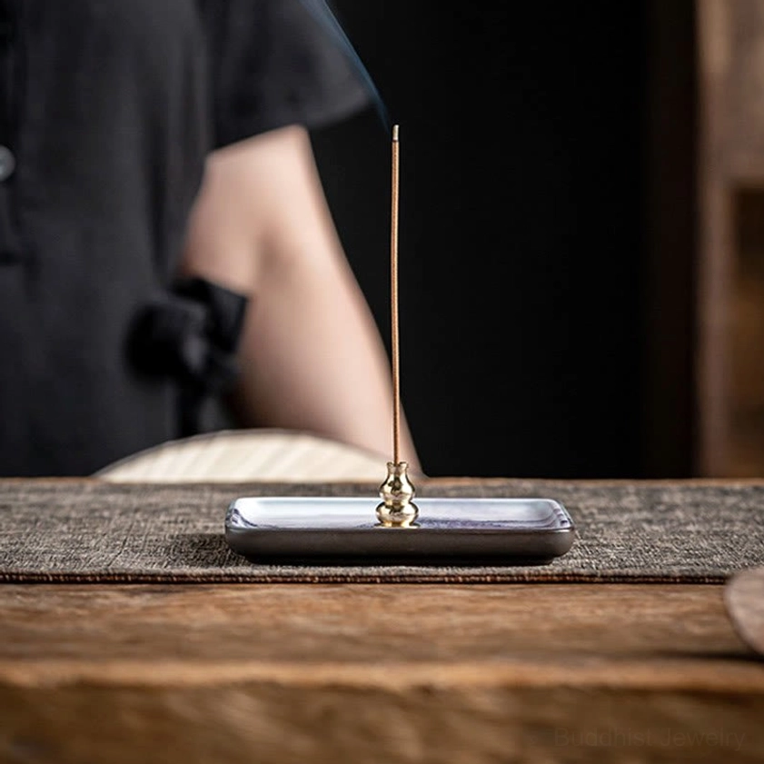Lit stick incense burning in ceramic incense burner tray with rising aromatic smoke on wooden tea table