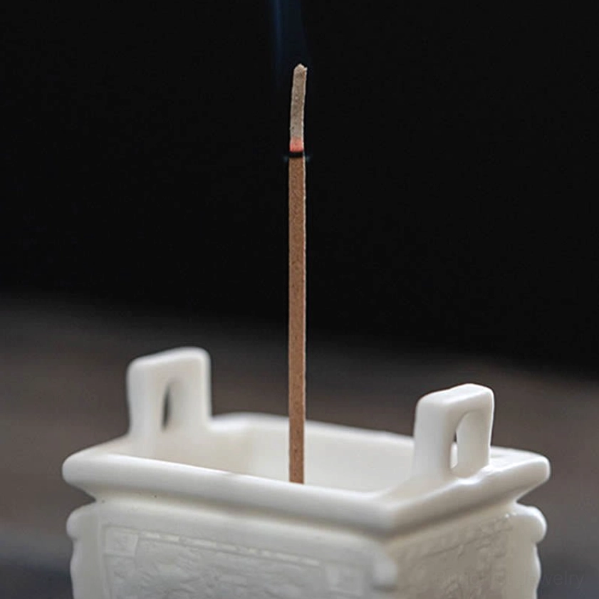 Buddhist ceramic incense burner with carved side patterns and tall burning incense, dark background studio photography