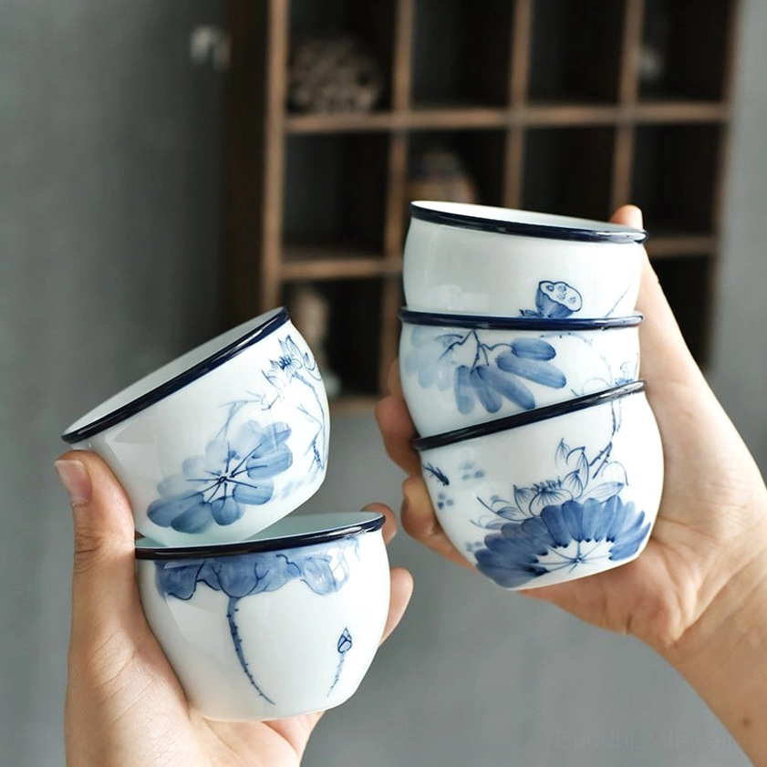 Hand-held ceramic teacup with blue floral and lotus motifs, close-up detail showing glaze quality and design