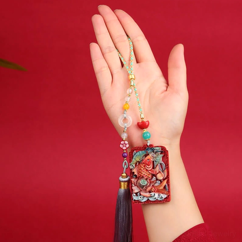 Handcrafted cinnabar koi lotus pendant showing intricate carving of koi fish and lotus flower patterns with natural stone texture