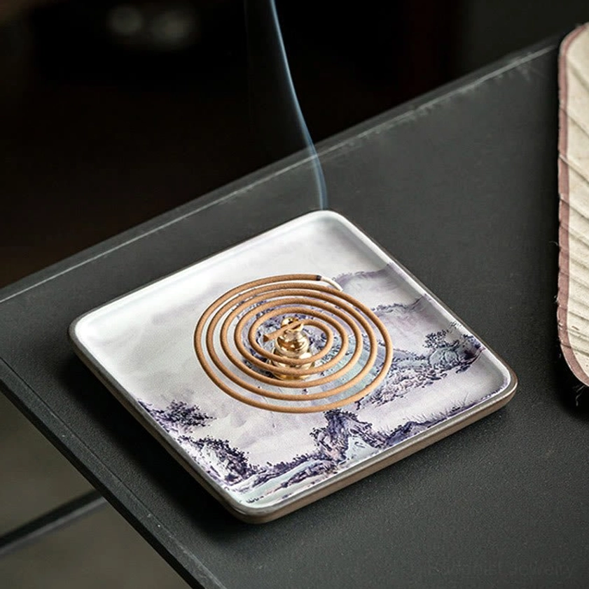 Lit coil incense with rising smoke in ceramic Buddhist burner tray on dark modern tabletop surface
