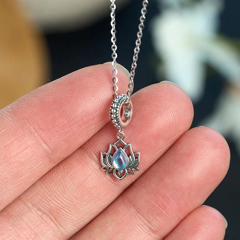 Close-up of lotus moonstone necklace pendant being held on fingertip showing intricate engraved detail and moonstone gemstone