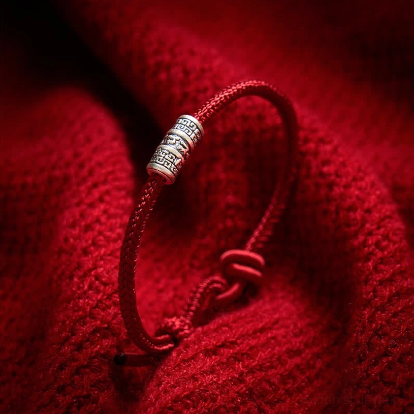 Handcrafted red cord Buddhist string bracelet with silver mantra bead, artisanal craftsmanship close-up