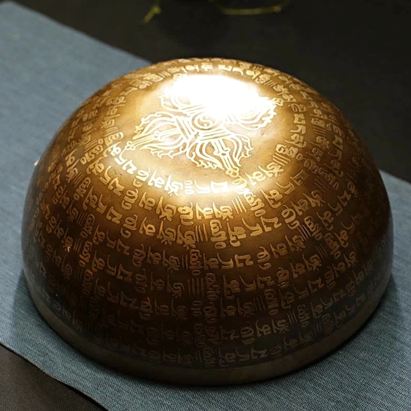 Upside-down handcrafted singing bowl showing engraved Buddhist scriptures and relief pattern