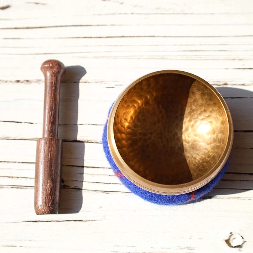 Overhead flat lay of authentic handcrafted singing bowl with dark wood mallet striker on white wooden table, showing bowl's textured surface and acoustic properties