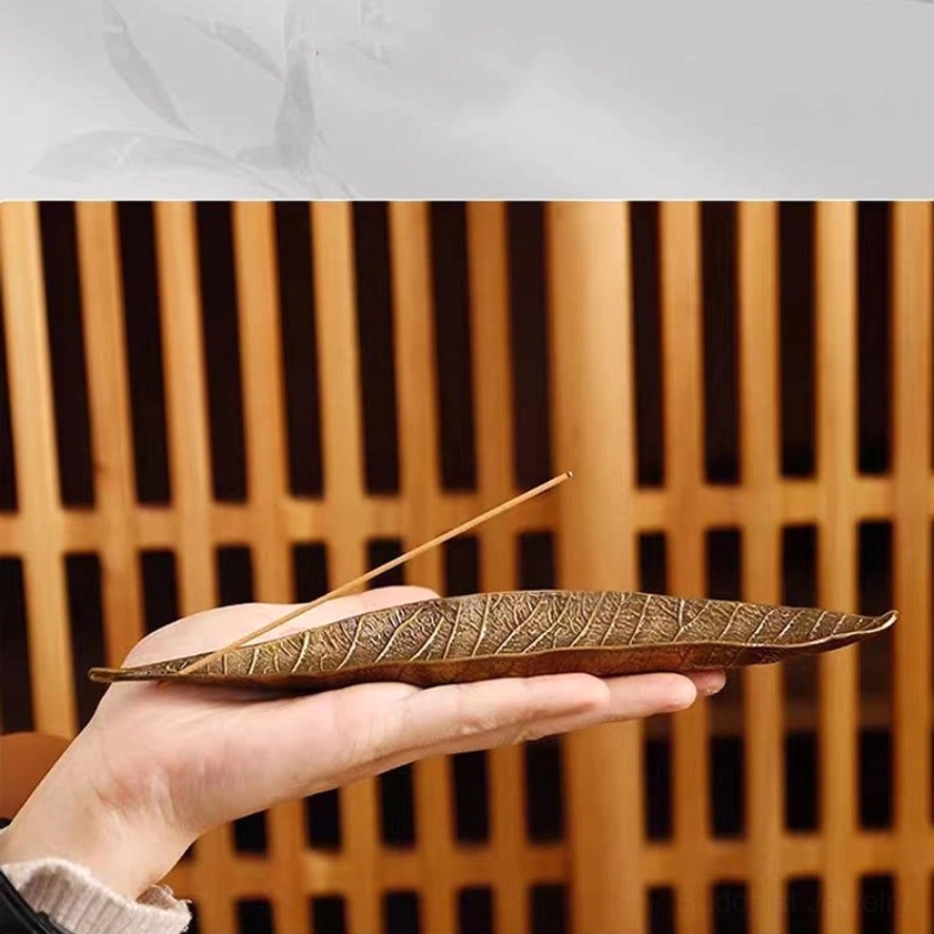 Hand-held bronze leaf incense burner with incense stick against wooden screen background