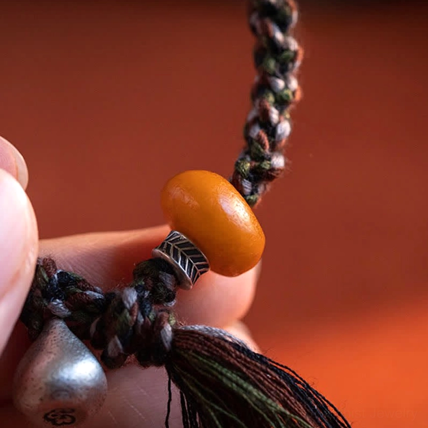 Handcrafted Buddhist amber bracelet showing artisanal braided rope and silver charm details