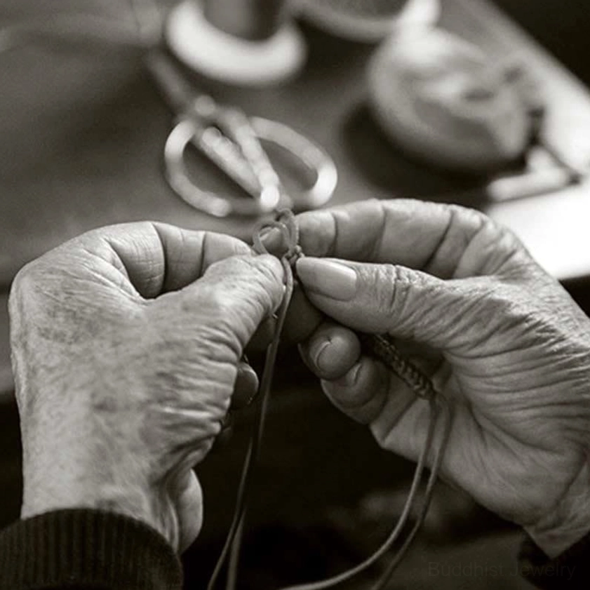 Artisan hands demonstrating traditional knotting and weaving technique for handmade Buddhist bracelet, black and white craft heritage image