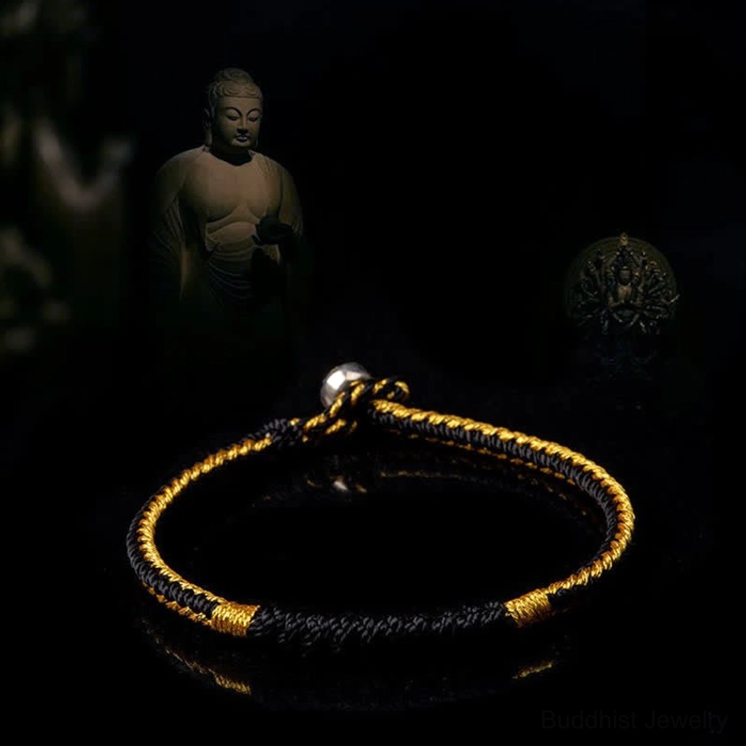 Black and gold braided Buddhist protection bracelet with woven design and metal clasp on dark spiritual background
