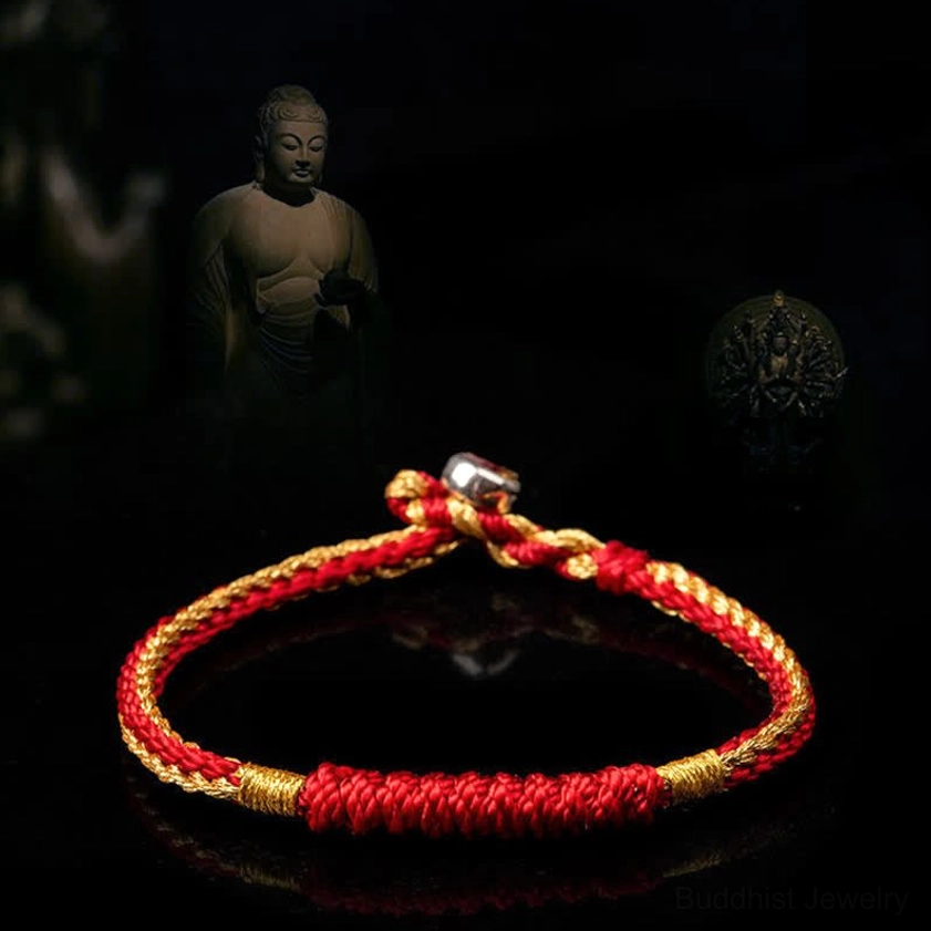 Single red and gold braided Buddhist string bracelet with metal clasp, top-down view on spiritual Buddha backdrop