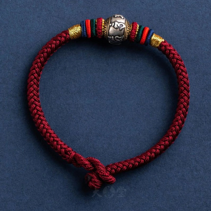 Handmade Buddhist braided bracelet featuring deep red rope, silver Om Mani Padme Hum charm, colorful decorative wraps, and slip-knot clasp
