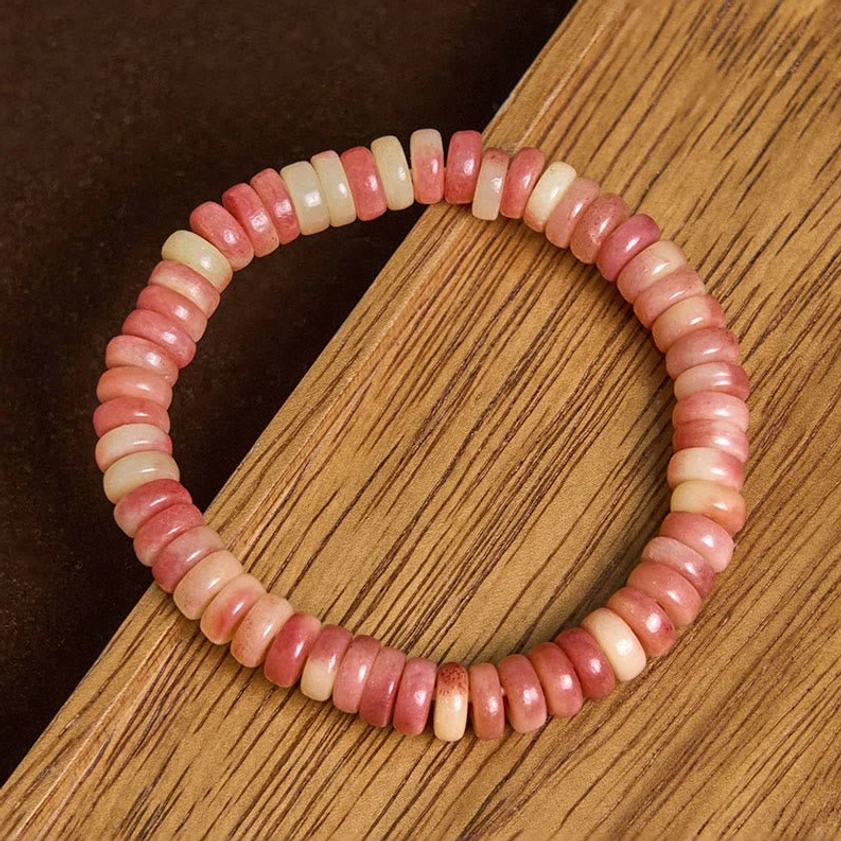 Two-tone pink and cream camel bone beaded bracelet with simple elastic design, overhead angle view on dark wooden background