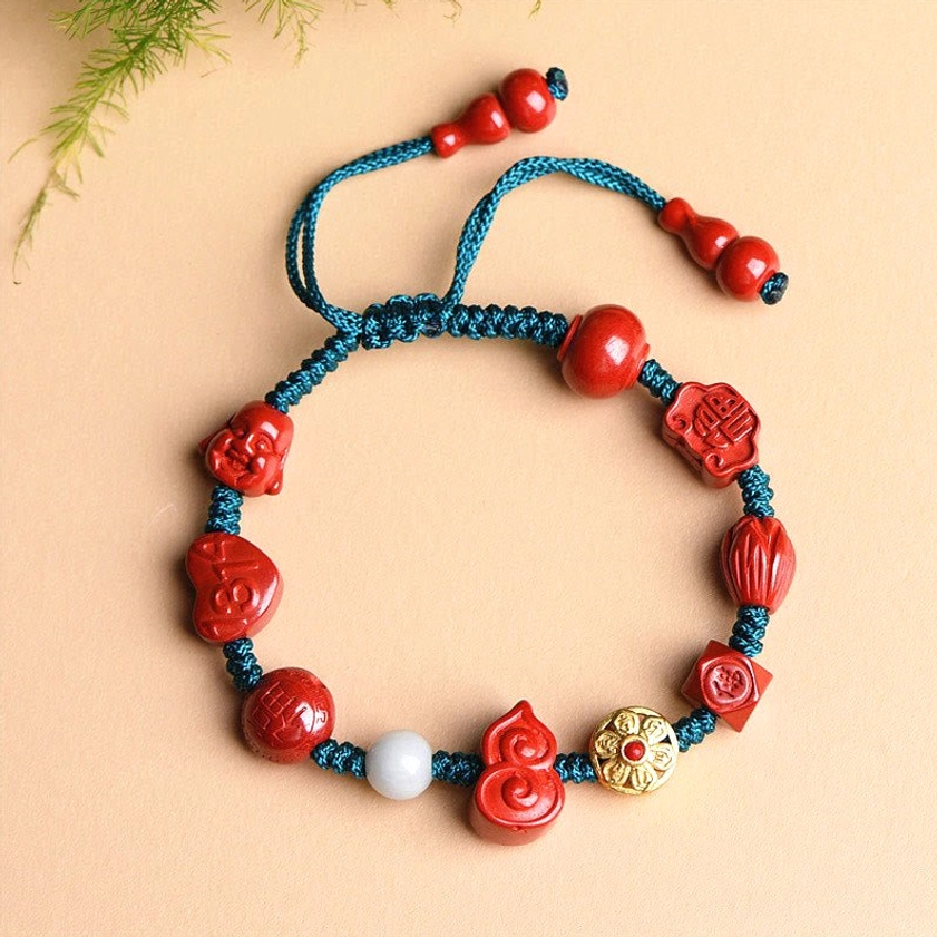 Three-quarter view of handmade cinnabar Buddhist bracelet featuring red carved beads, gourd pendant, and teal braided cord