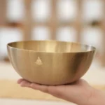 Handmade copper singing bowl held in palm, showing warm golden brass finish and authentic artisan craftsmanship details