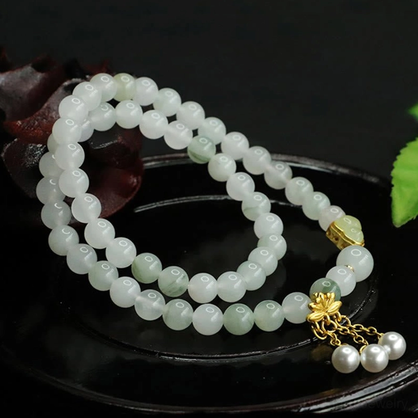 Handmade Tianshan jade lotus double circle bracelet with white pearl charms and gold accent on wooden base with natural green leaf