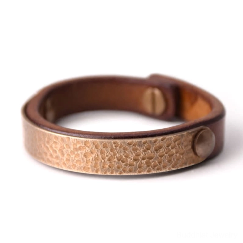 Artisan leather and brass Buddhist prosperity bangle featuring hammered texture and bronze hardware against white background