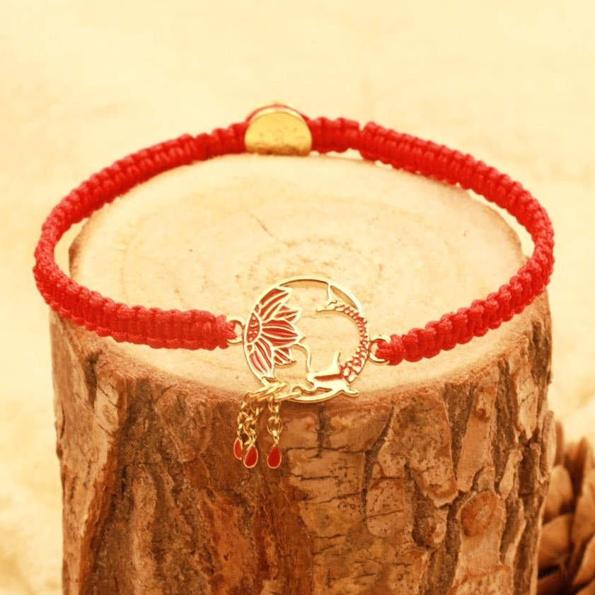 Handmade lotus koi red string bracelet with gold clasp and dangling tassel charms on light wood surface