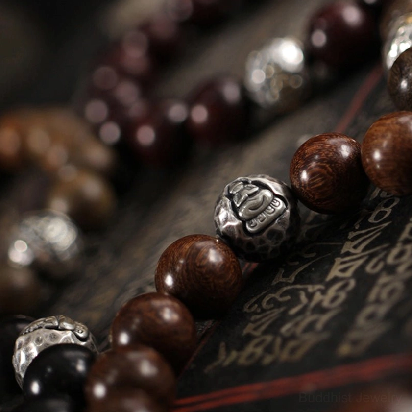 Multiple handmade sandalwood bracelets with sterling silver Buddha beads in mixed wood varieties, side-by-side close-up with vintage fabric background