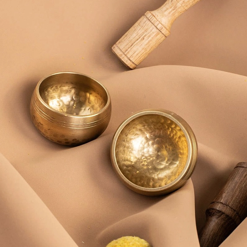 Handcrafted brass singing bowls with mixed-tone wooden mallets on soft fabric background
