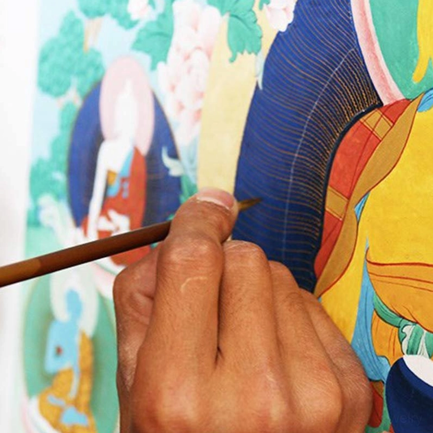 Hand-painted Thangka artwork in progress with artist's paintbrush and vibrant Buddhist spiritual designs on studio canvas