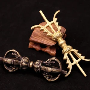 Collection of handmade brass and copper vajra dorje ornaments in various sizes, displayed on wooden stands against dark fabric background