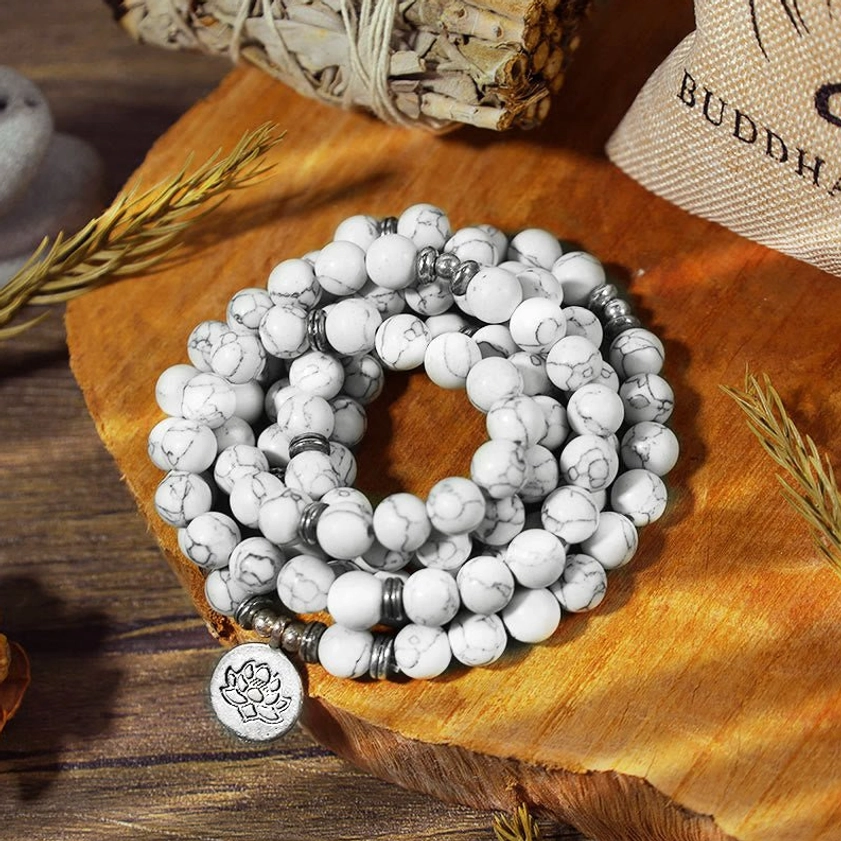 Natural white turquoise lotus mala bracelet laid flat on wooden surface with dried grass and brand pouch showing bead texture