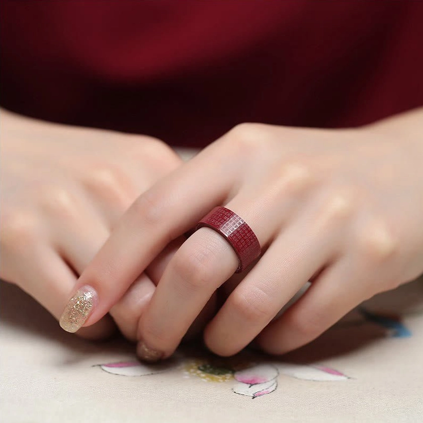 Two hands wearing cinnabar Buddhist engraved rings matte red finish side view on floral fabric background