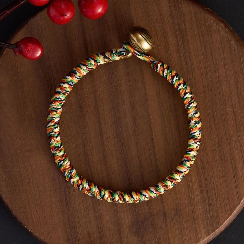 Full loop view of handwoven multicolor braided bracelet with decorative copper charm on wooden disc background