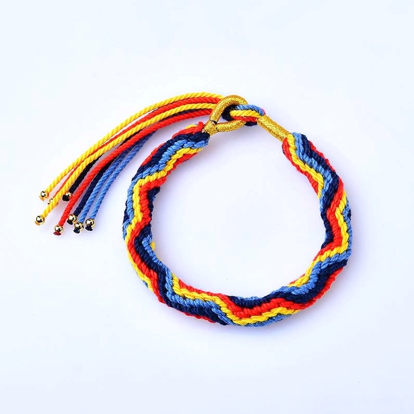 Overhead view of handmade multicolor braided lucky bracelet with chevron woven pattern in red blue yellow and gold tones, adjustable tassel straps on white background
