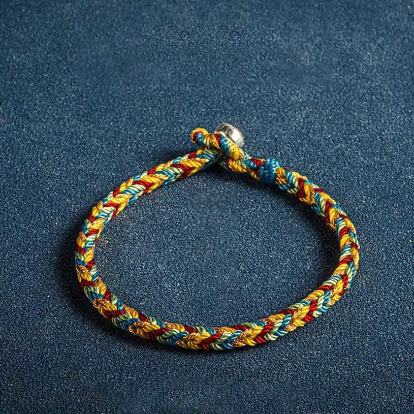 Single handwoven multicolored Buddhist protection bracelet with sterling silver toggle clasp, top-down close view on textured background