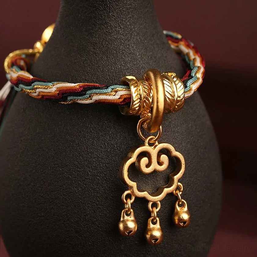 Close-up side view of Buddhist healing bracelet showing thick antique gold hardware, hollow cloud lock pendant with hanging bells and multicolor braided band