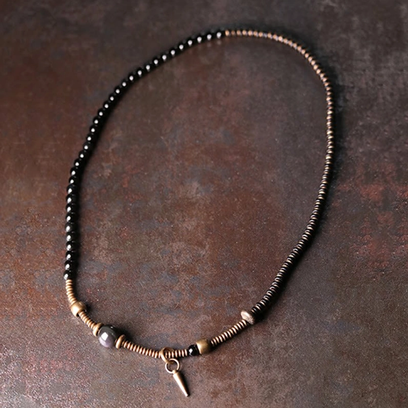 Flat lay of unfolded triple wrap healing bracelet showing single-strand laid-out beaded chain with central obsidian bead and cone pendant