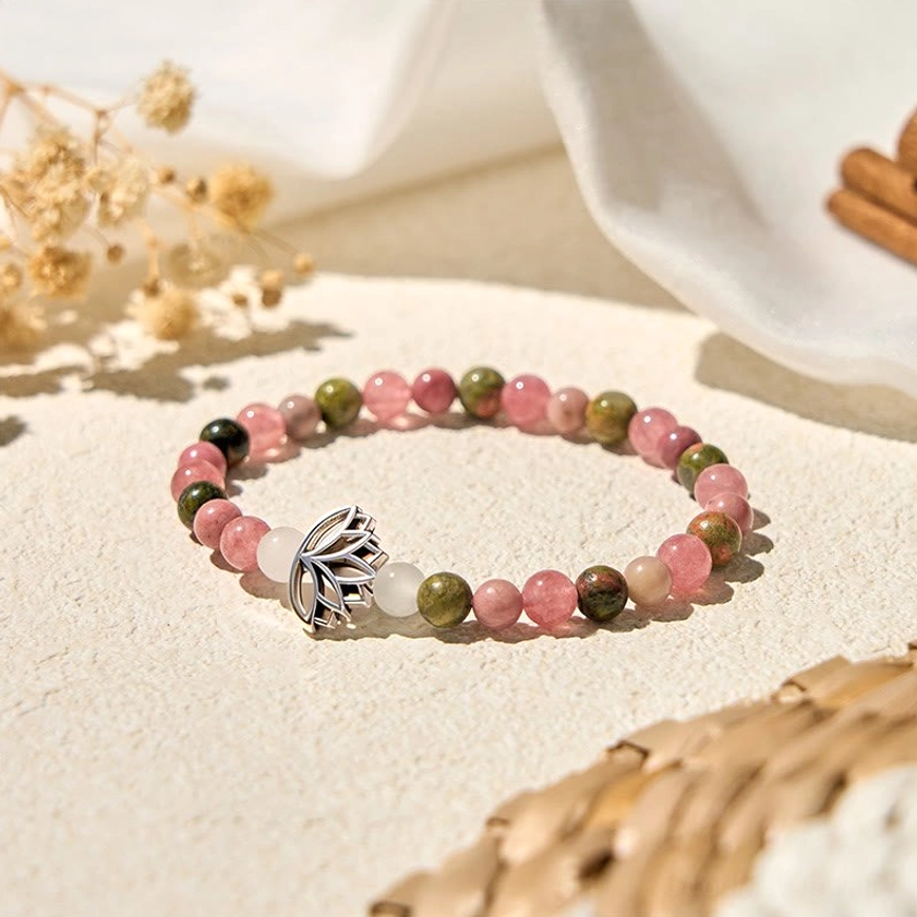 Pink and green natural stone beads with silver lotus charm elastic bracelet on beige textured surface