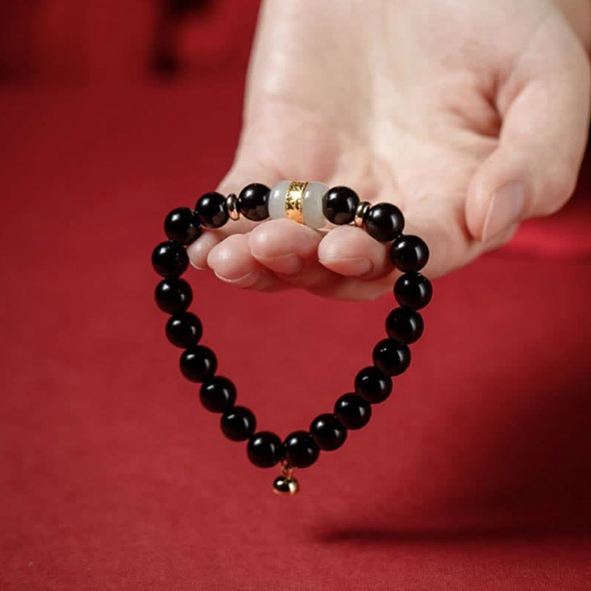 Black obsidian and jade heart-shaped bracelet formation with tiny hanging charm held in palm against red fabric background