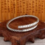 Retro Heart Sutra twisted copper bangle with engraved Buddhist characters displayed on wooden stand with bamboo script background, showing flat lay perspective