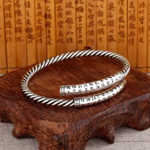 Retro Heart Sutra twisted copper bangle with engraved Buddhist characters displayed on wooden stand with bamboo script background, showing flat lay perspective