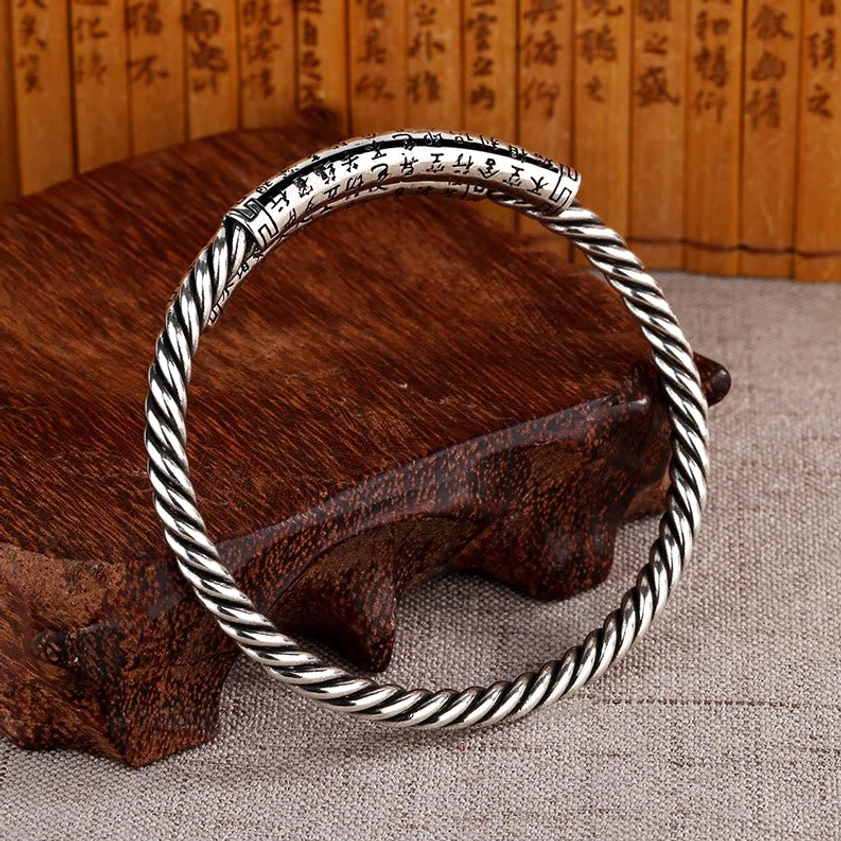 Single adjustable copper Heart Sutra bangle with open cuff design and twisted metal texture, side profile flat view on wooden stand