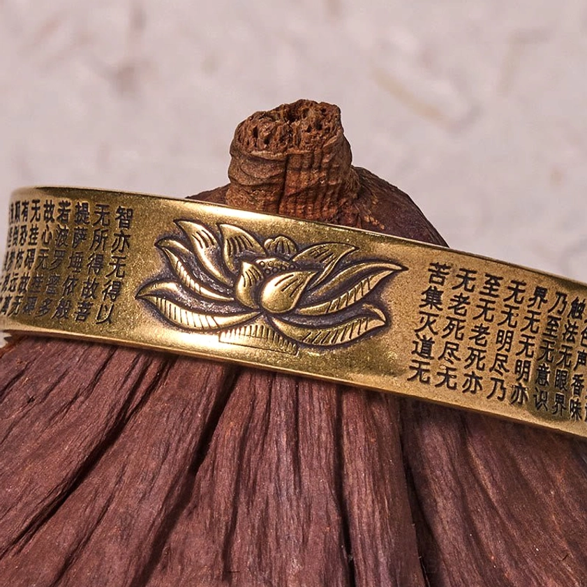Heart Sutra brass bangle bracelet with bronze metal finish showing lotus relief and surrounding sutra text, styled with spiritual props